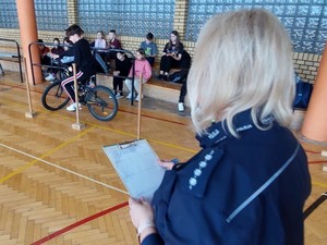 Policjantka będzińskiej drogówki trzyma kartę punktową i ocenia przejazd dziecka na rowerze.