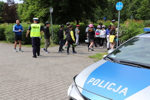 Radiowóz policyjny znajduje się po prawej stronie fotografii, dalej widzimy policjantów oprowadzających po rowerowej trasie.