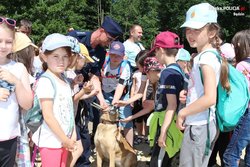 Grupa dzieci która otacza policjanta  oraz przewodnika psa.