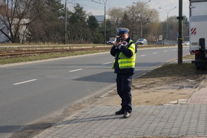 Policjant stojący przy drodze z miernikiem prędkości.