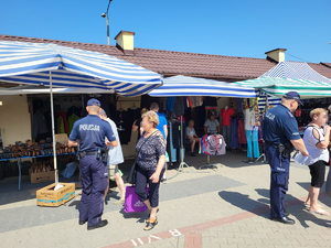 Dzielnicowi rozdają ulotki profilaktyczne przechodniom na targowisku miejskim.