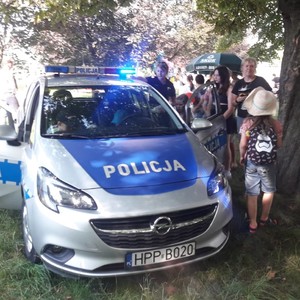 Policjanci podczas spotkania z młodzieżą na wolnym powietrzu przy radiowozie.