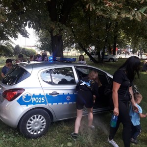 Policjantka pokazuje dzieciom jak wygląda policyjny radiowóz i zaprasza ich do środka.