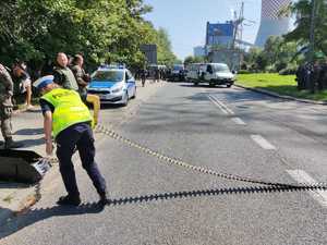 Policjantka rozkłada kolczatkę na jezdni w tle radiowóz i inne samochody na jezdni.