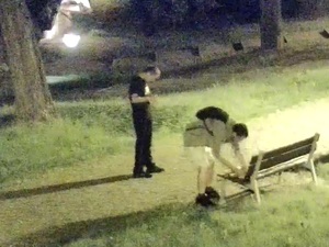 Dwóch mężczyzn w parku, jeden opiera nogę o ławkę, a drugi stoi.