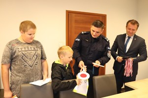 Pierwszy Zastępca Komendanta Powiatowego Policji w Będzinie wraz ze Starostą Będzińskim przekazują dzieciom atrybuty do pełnienia służby.