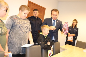 Starosta Będziński wraz z Pierwszym Zastępcą Komendanta Powiatowego Policji w Będzinie  przekazują dzieciom atrybuty do pełnienia służby.