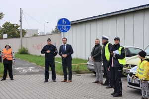Pierwszy Zastępca Komendanta Powiatowego Policji w Będzinie wraz ze Starostą Będzińskim i innymi uczestnikami akcji stoją na parkingu.