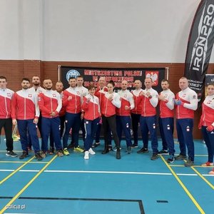 Grupa osób ubranych w biało-czerwonych dresach pozuje do zdjęcia na hali sportowej.