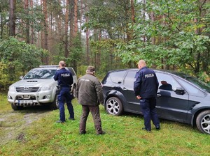 Policjanci i strażnicy leśni podczas wykonywania czynności służbowych w lesie stoją obok samochodu.