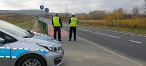 Dwóch policjantów stoi przy drodze, na pierwszym planie widoczny radiowóz.