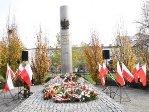 Pomnik Poległym Za Wolną Polskę, pod nim ustawione są złożone kwiaty i biało-czerwone kwiaty.