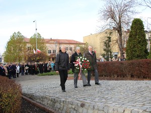Trzech mężczyzn idą z kwiatami, celem złożenia pod pomnikiem.