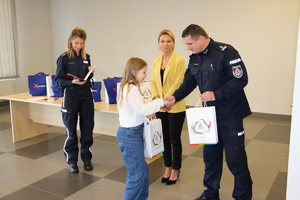Zastępca Komendanta Powiatowego Policji w Będzinie w obecności Pani Wiceprezydent będzina i policjantki wręcza nagrodę dziewczynce.