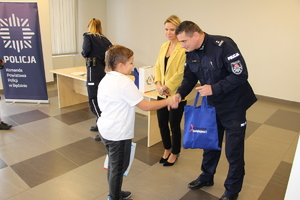 Zastępca Komendanta Powiatowego Policji w Będzinie w obecności Pani Wiceprezydent będzina i policjantki wręcza nagrodę chłopcu.