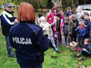 Na zdjęciu policjantka stoi przed grupą dziećmi na trawniku.