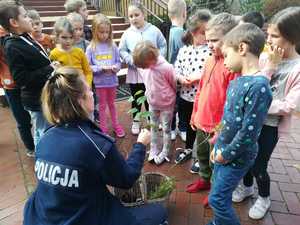 Zdjęcie przedstawia policjantkę, która pokazuje grupie dzieci małe drzewka do sadzenia.