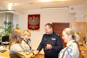 Na zdjęciu harcerki przekazują Komendantowi Powiatowemu Policji w Będzinie światełko betlejemskie w gabinecie.