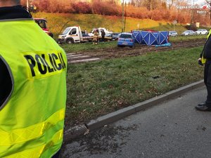 Na zdjęciu po lewej stronie widoczna odblaskowa kamizelka policyjna, dalej widać niebieski samochód oraz parawan policyjny i strażacki