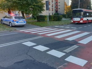 Radiowóz z włączonymi sygnałami świetlnymi przy przejściu dla pieszych, gdzie przejeżdża autobus.
