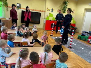 Policjantka pokazuję imitację znaku drogowego grupie dzieci w sali przedszkola.