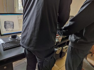 Na zdjęciu technik kryminalistyki pobiera odciski palców od zatrzymanego mężczyzny.