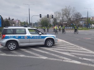 Na zdjęciu radiowóz policyjny, obok którego przejeżdżają rowerzyści.