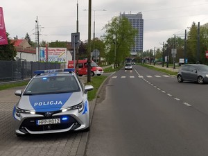 Na zdjęciu radiowóz policyjny, który ustawiony jest przy drodze. Z tyłu widzimy inne samochody, w tym wóz strażacki.