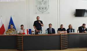 Zdjęcie przedstawiające grupę uczestników debaty, którzy ją prowadzą, przy mikrofonie Komendant Powiatowy Policji w Będzinie inspektor Arkadiusz Więcek.