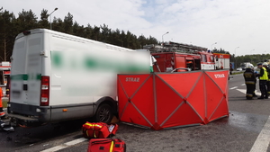 Na zdjęciu samochów iveco, który uderzył w wóz strażacki, obok znajduje się czerwony parawan oraz osoby, które wykonują czynności na miejscu zdarzenia.