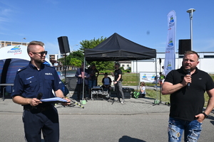 Na zdjęciu policjant i mężczyzna z mikrofonami przemawiają podczas organizowanego wydarzenia.