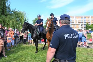 Na zdjęciu policjant z mikrofonem opowiada o pracy policji konnej. Policjanci na koniach prezentują się podczas pikniku,