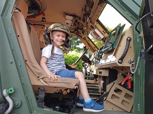Na zdjęciu dziecko w pojeździe wojskowym i założonym kaskiem.