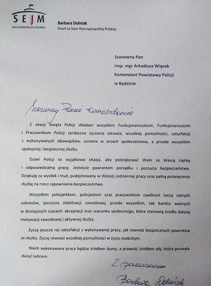 Zdjęcie przedstawia podziękowania od Posła na Sejm Barbary Dolniak: Szanowny Pan inspektor magister Arkadiusz Więcek Komendant Powiatowy Policji w Będzinie. Szanowny Panie Komendancie. Z okazji Święta Policji składam wszystkim Funkcjonariuszkom, Funkcjonariuszom i Pracownikom Policji serdeczne życzenia zdrowia, wszelkiej pomyślności, satysfakcji z wykonywanych obowiązków, uznania w oczach społeczeństwa, a przede wszystkim spokojniej i bezpiecznej służby. Dzień Policji to wyjątkowa okazja, aby podziękować Wam za Waszą ciężką i odpowiedzialną pracę. Jesteście gwarantem porządku i poczucia bezpieczeństwa. Dziękuję za wysiłek i trud, podejmowany w Waszej codziennej pracy oraz pełną poświęcenia służbę na rzecz zapewnienia bezpieczeństwa. Wszystkim policjantkom, policjantom oraz pracownikom cywilnym życzę samych sukcesów, poczucia stabilizacji zawodowej, przede wszystkim, tak bardzo ważnych w dzisiejszych czasach: akceptacji oraz szacunku społecznego, które stanowią Źródło dalszej motywacji zawodowej i aktywnej służby. Życzę jeszcze raz satysfakcji z wykonywanej pracy, jak również bezpiecznych powrotów ze służby. Życzę również wszelkiej pomyślności w życiu osobistym. Niech wykonywana praca będzie Źródłem durny, a prawość źródłem siły, która pozwala służyć ludziom.