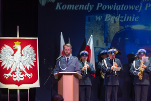 Na zdjęciu policjant przemawiający na mównicy, za nim policjanci orkiestry policyjnej.