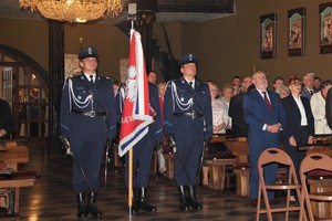 Zdjęcie przedstawiające Sztandar Komendy Wojewódzkiej Policji w Katowicach, który znajduje się w kościele. Na zdjęciu widać również innych uczestników Mszy Świętej.