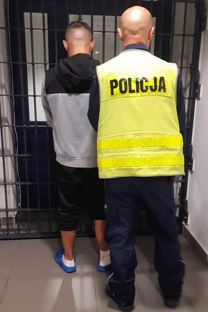 Na zdjęciu policjant stoi z zatrzymanym przed policyjnym aresztem.