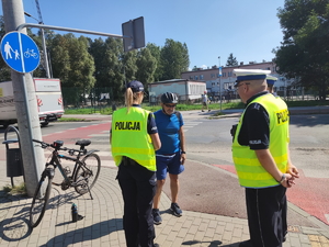 Zdjęcie. Policjanci z policjantką stoją z rowerzystą przy przejściu dla pieszych i rozmawiają.