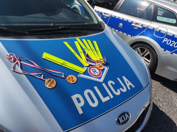 NA zdjęciu widzimy odblaski i medale wzorowego kierowcy rozłożone na masce policyjnego radiowozu.