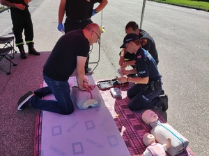 Na zdjęciu mężczyzna ćwiczy na fantomie z policjantką i strażakiem podczas kursu pierwszej pomocy.