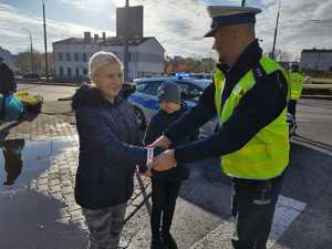 Zdjęcie, na którym policjant zakłada kobiecie z dzieckiem opaskę odblaskową.