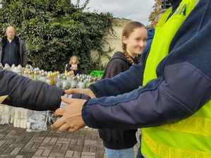 Zdjęcie, na którym policjant zakłada osobie opaskę odblaskową, w tle widać osoby sprzedające znicze.