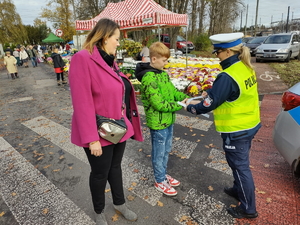 Zdjęcie. Policjantka przy terenie cmentarza zakłada chłopcu opaskę odblaskową.