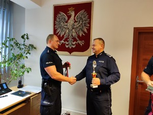 Na zdjęciu Komendant Powiatowy Policji w Będzinie inspektor Arkadiusz Więcek gratuluje policjantowi i podaje mu rękę w swoim gabinecie.