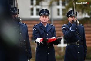 Na zdjęciu policjant trzyma w rękach flagę w asyście innych policjantów.