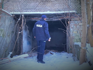 Zdjęcie. Policjant stoi przed opuszczonym budynkiem.