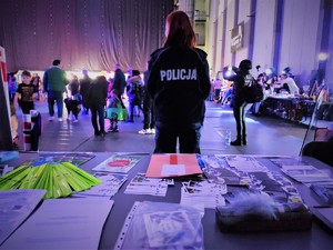 Na zdjęciu widzimy gadżety policyjne oraz policjantkę, która stoi przed stołem.