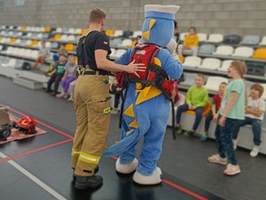 Na zdjęciu strażak ubiera w kamizelkę maskotkę policyjną.