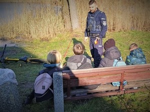 Na zdjęciu policjant rozmawia z 4 chłopcami przy zbiorniku wodnym.