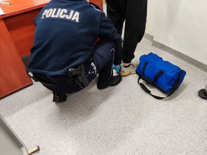 Na zdjęciu policjant zakłada kajdanki zatrzymanemu na nogi.